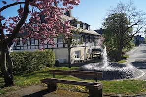 Ein traditionelles Gebäude mit einem Brunnen, einer Bank und einem Baum mit rosa Blüten.