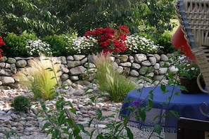 Ein Garten mit Steinmauer, verschiedenen Pflanzen und einem Tisch mit blauer Tischdecke.