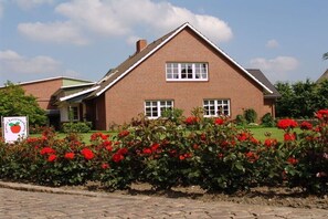 Una casa de ladrillo con techo inclinado, dos ventanas y un jardín con flores rojas.