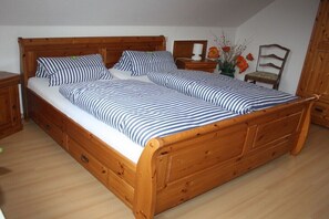 Una cama de madera con ropa de cama a rayas, una mesita de noche, una silla y un florero con flores.