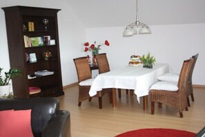 Un comedor con una mesa, sillas, una estantería y una lámpara colgante.