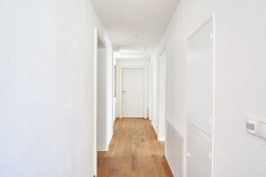 Ein schmaler Flur mit weißen Wänden und Holzböden, der zu einer verschlossenen Tür am Ende führt.