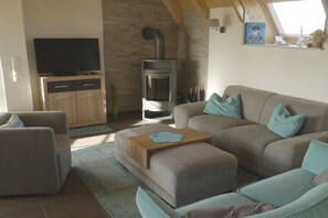 Ein Wohnzimmer mit Sofa, Hocker, Fernseher und Kaminofen.