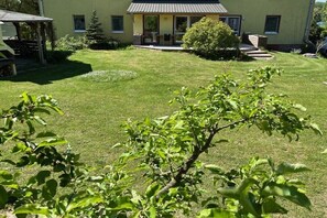 Ein Haus mit gepflegtem Rasen, einer Veranda mit Gartenmöbeln und einem kleinen Baum im Vordergrund.