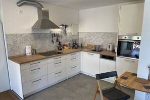 Eine moderne Küche mit weißen Schränken, einer Marmor-Spritzschutzwand und einem eingebauten Backofen.