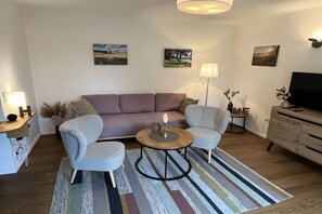 Ein Wohnzimmer mit einer Couch, zwei Sesseln, einem Couchtisch, einer Lampe und einem Fernseher.