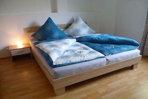 Ein Bett mit Holzrahmen, ein Nachttisch mit Schublade und eine Nachttischlampe.