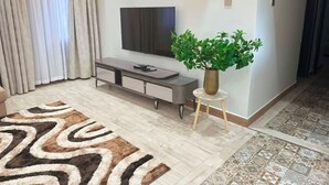 Ein modernes Wohnzimmer mit Flachbildfernseher, einer Couch, einem Couchtisch, einem gemusterten Teppich und einem Blumentopf.
