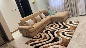Ein Wohnzimmer mit einem beigefarbenen Ecksofa, einem gemusterten Teppich und einer schwarzen Tür.