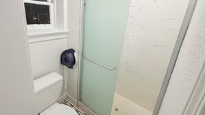 Een badkamer met een toilet, een douche met een glazen deur en een raam met uitzicht.
