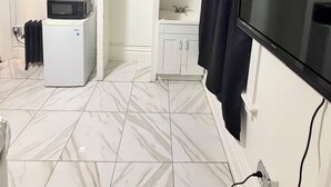 Een kamer met een witte koelkast, een magnetron, een flatscreen-tv, een witte wastafel en een deur naar een andere kamer.