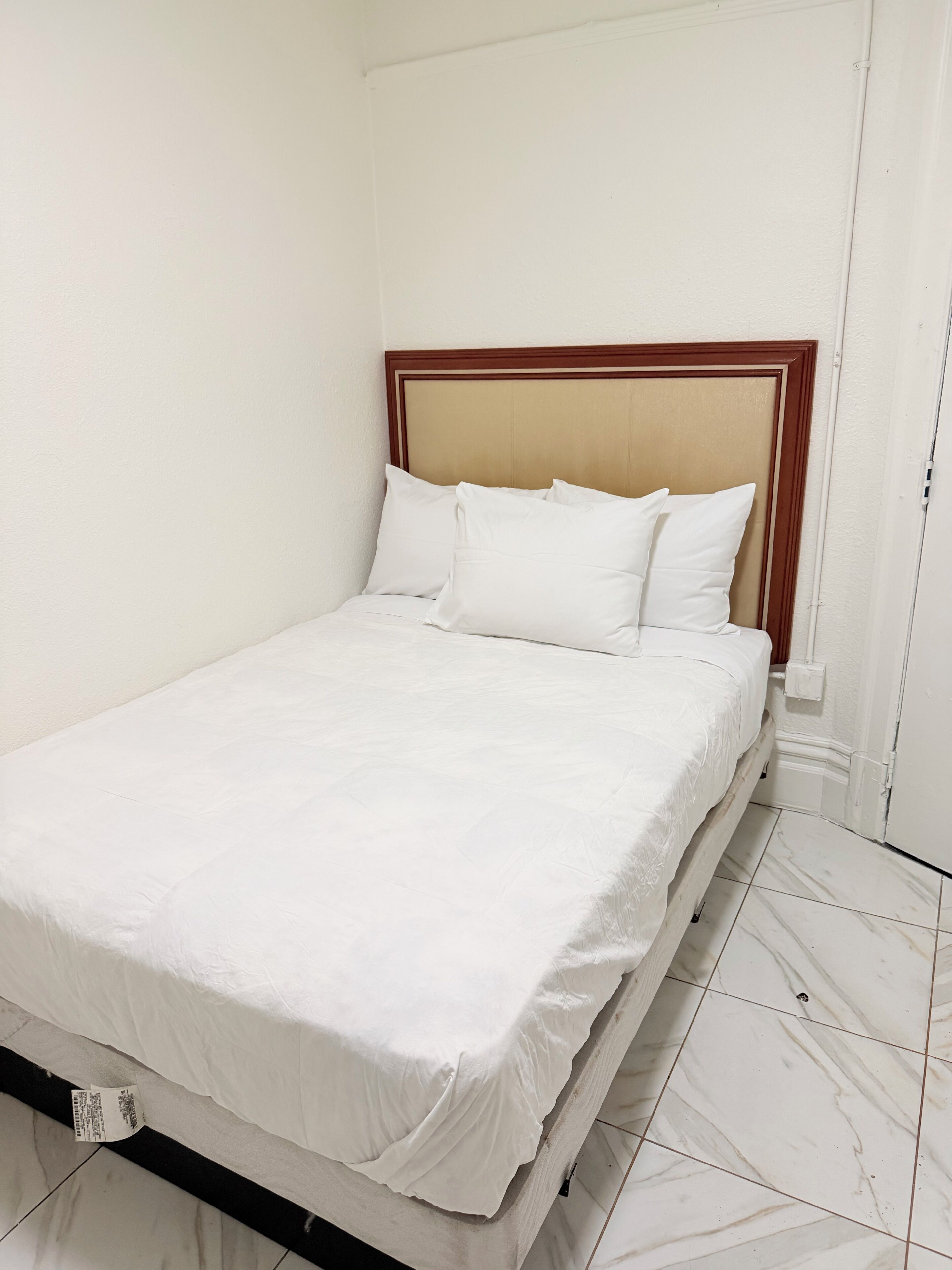 A single bed with a wooden headboard, white bedding, and a tiled floor.