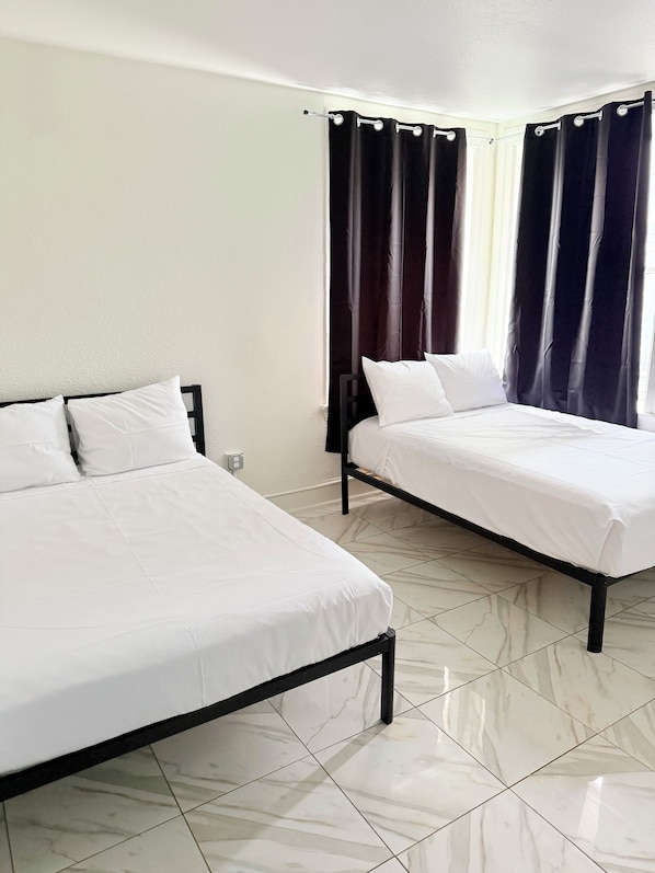A hotel room with two beds, a window with curtains, and a tiled floor.