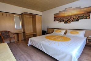 Ein Schlafzimmer mit Bett, Sessel, Kleiderschrank, Nachttisch und einer Wand mit einem Sonnenblumenbild.