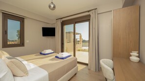 A hotel room with a bed, a desk, a chair, a TV, and a view of the outdoors. - Alekos Beach Houses-Glafki Villa (Kefalonia)