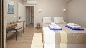 A hotel room with a bed, a desk, a chair, a small stool, and a painting on the wall. - Alekos Beach Houses-Aelia Villa (Kefalonia)