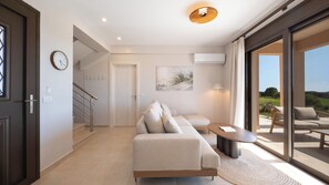 A modern living room with a sofa, a coffee table, and a view through glass doors to an outdoor area. - Alekos Beach Houses-Aelia Villa (Kefalonia)