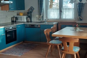 A kitchen with blue cabinets, a stove, a microwave, and a sink. There is a dining table with chairs and a window with curtains. - Holiday apartment with 2 bedrooms (Rauris)