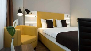 Hotellihuone, jossa on sänky, tuoli, pieni pöytä ja lamppu.