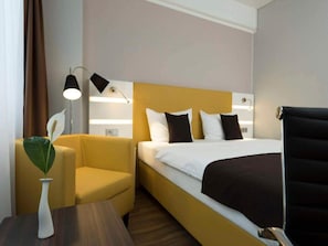 Une chambre d’hôtel avec un lit, une chaise, une petite table et une lampe.