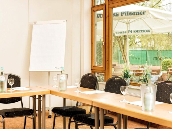 A conference room with a whiteboard, tables with chairs, and a view of an outdoor area with umbrellas.