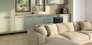 A modern kitchen with light green cabinets, a beige sofa, and a window with a view of greenery. - Alekos Beach Houses-Nereids Villas (Kefalonia)