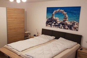 Ein Schlafzimmer mit einem Bett, einem Holzschrank, einem Nachttisch, einer Lampe und einem Gemälde einer Felsbogen über Wasser.