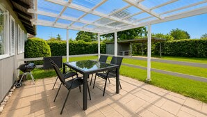 A covered patio with a glass table and chairs, a barbecue grill, and a view of a green lawn and trees. - Nice home in Sydals with WiFi (Sydals)