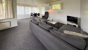 A modern living room with a grey sofa, a TV, and a dining area with a table and chairs. - Nice home in Sydals with WiFi (Sydals)