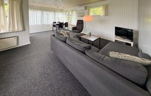 Ein modernes Wohnzimmer mit grauem Sofa, Fernseher und Essbereich mit Tisch und Stühlen.