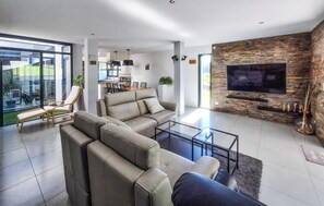 A modern living room with a sectional sofa, a glass coffee table, a flat-screen TV mounted on a stone wall, and a dining area in the background. - Cozy home in Bassens with WiFi (Bassens)
