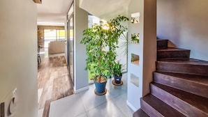 Un interior moderno con una escalera, plantas en macetas y vistas a una sala de estar.