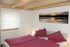 Ein Schlafzimmer mit einem Bett, einem Fenster mit Jalousien, einem Wandbild und einer Nachttischlampe.