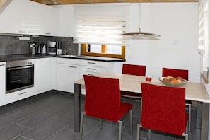 Eine moderne Küche mit weißen Schränken, einem eingebauten Ofen und einem Essbereich mit roten Stühlen und einem Holztisch.