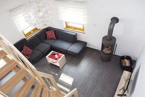 Ein modernes Wohnzimmer mit grauem Sofa, roten Kissen, einer weißen Designleuchte, einem Kamin und einer Holztreppe.