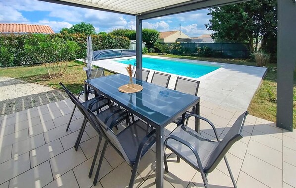 Eine Terrasse im Freien mit einem Glastisch und Stühlen, ein Pool im Hintergrund und Blick auf eine Wohngegend.