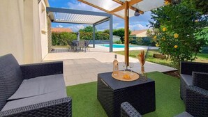 An outdoor patio with wicker furniture, a table with a bottle and glasses, and a view of a swimming pool and greenery. - Awesome home in Soubise (Soubise)