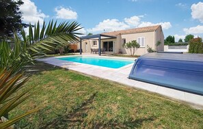 Ein Schwimmbecken, ein überdachter Grill und ein Haus mit einem Ziegeldach.