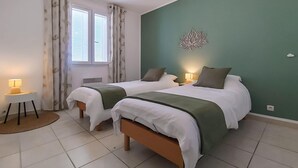 A room with two beds, a small table with a lamp, a window with curtains, and a wall decoration. - Awesome home in Soubise (Soubise)