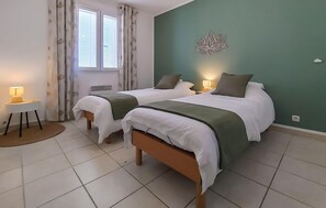 Une chambre avec deux lits, une petite table avec une lampe, une fenêtre avec des rideaux et un élément décoratif mural.