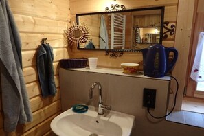 Ein Badezimmer einer Holzhütte mit Waschbecken, Spiegel, Handtuchhalter und einem Wasserkocher auf der Ablagefläche.