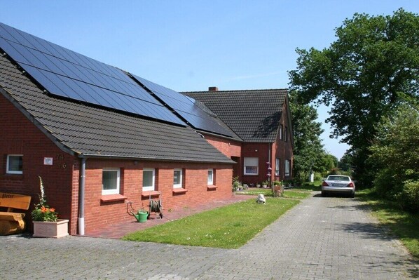 Une maison en briques rouges, dotée de panneaux solaires sur le toit, avec une allée pavée et une voiture garée dans la rue.