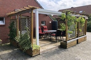 Un patio couvert avec une table et des chaises, une pergola en bois et des plantes grimpantes.