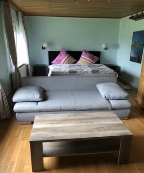 Ein Zimmer mit einer Couch, einem Bett mit bunten Kissen, einem Nachttisch und einer Holzbalkendecke.