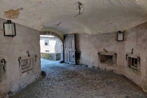 Ein rundbogiger Durchgang führt in einen Kopfsteinpflasterhof mit Steinmauern und einem rustikalen, historischen Gebäude im Hintergrund.