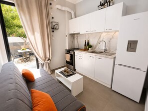 Eine moderne Küche mit weißen Schränken, einem eingebauten Backofen und einem Spülbecken. Es gibt eine Essecke mit Tisch und Stühlen, sowie eine Couch mit orangenen Kissen.