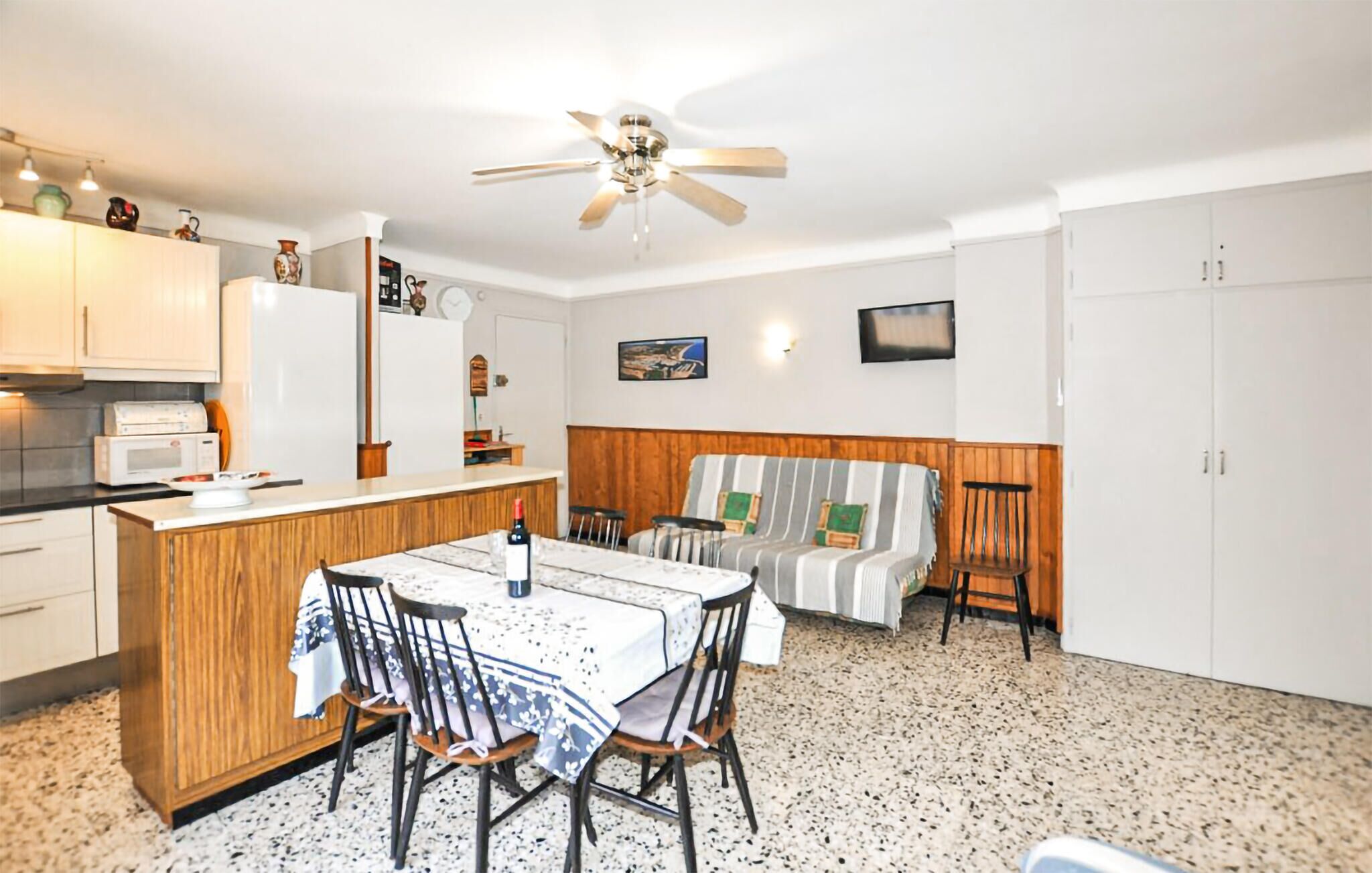 A compact kitchen with a dining area, a ceiling fan, and a TV mounted on the wall.