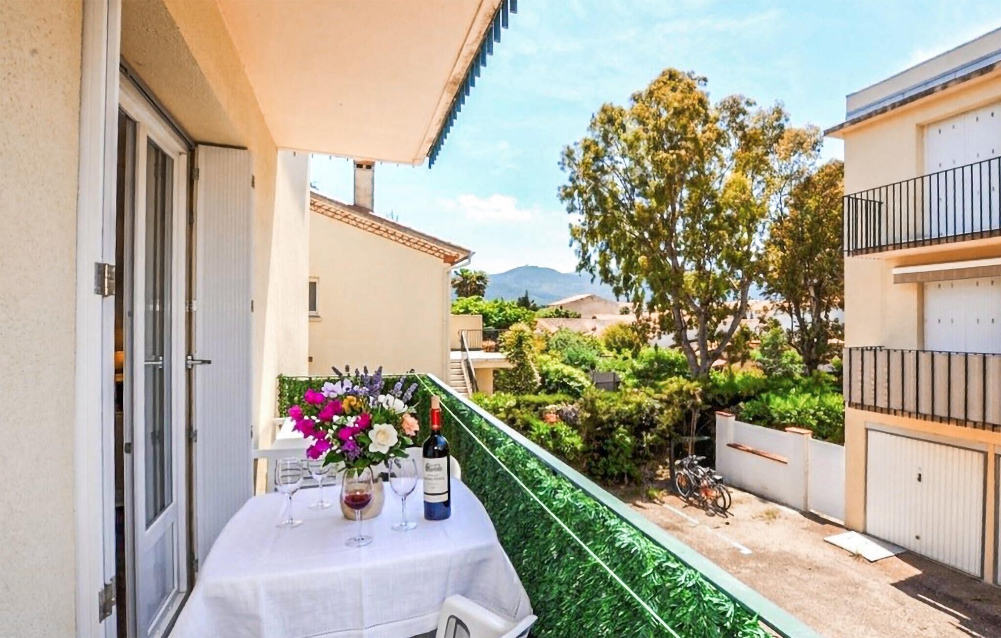 Een balkon met een eettafel, omgeven door groen en uitzicht op de omgeving.