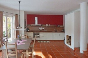 Een keuken met witte kasten, een rode accentmuur, en een eethoek met een tafel en stoelen.