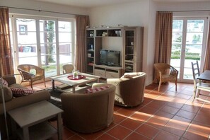 Een woonkamer met een bank, stoelen, een televisie en een eettafel.